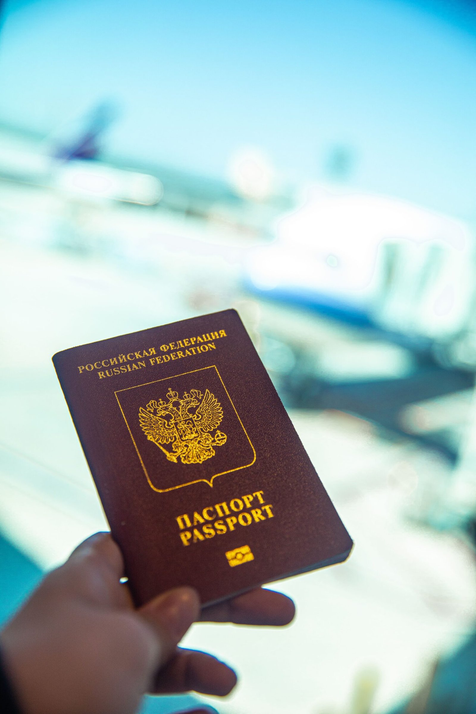 Close-up of a passport held near an airport gate window with blurred aircraft visible in the background
