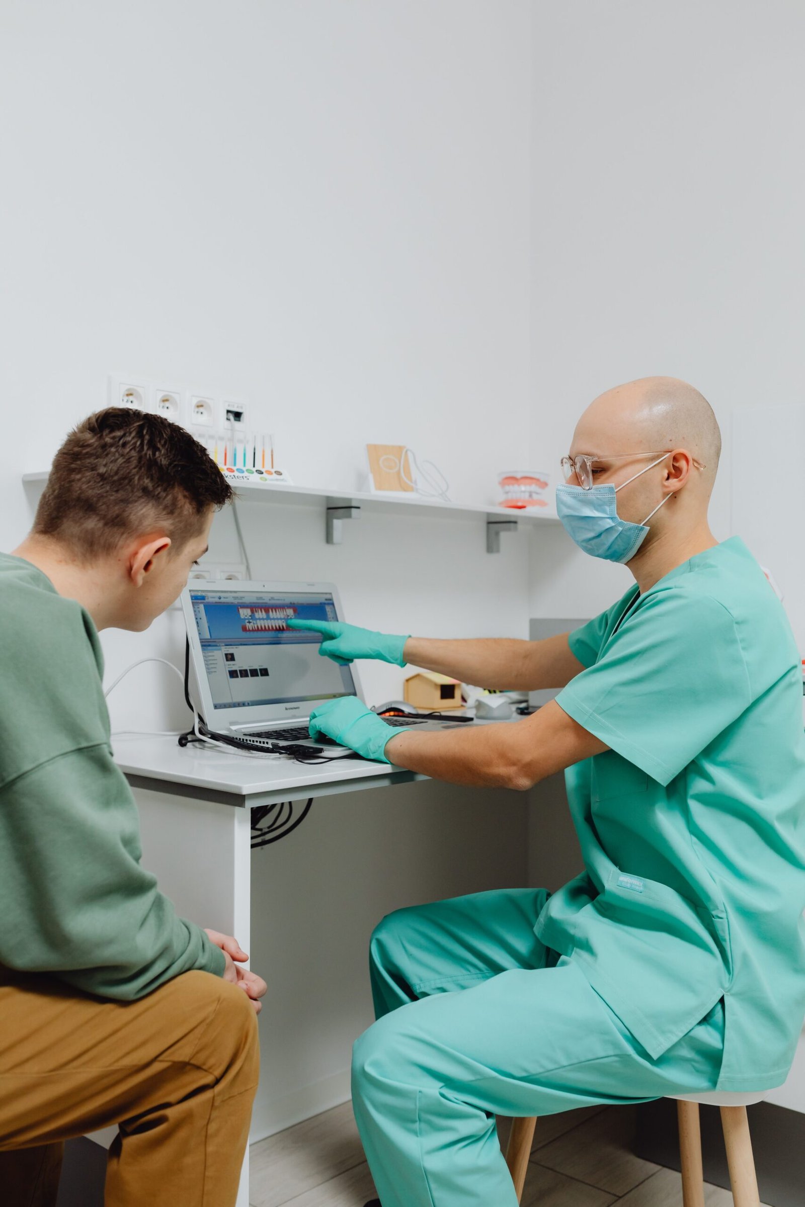 A dentist consulting a patient while showing dental information on a laptop screen