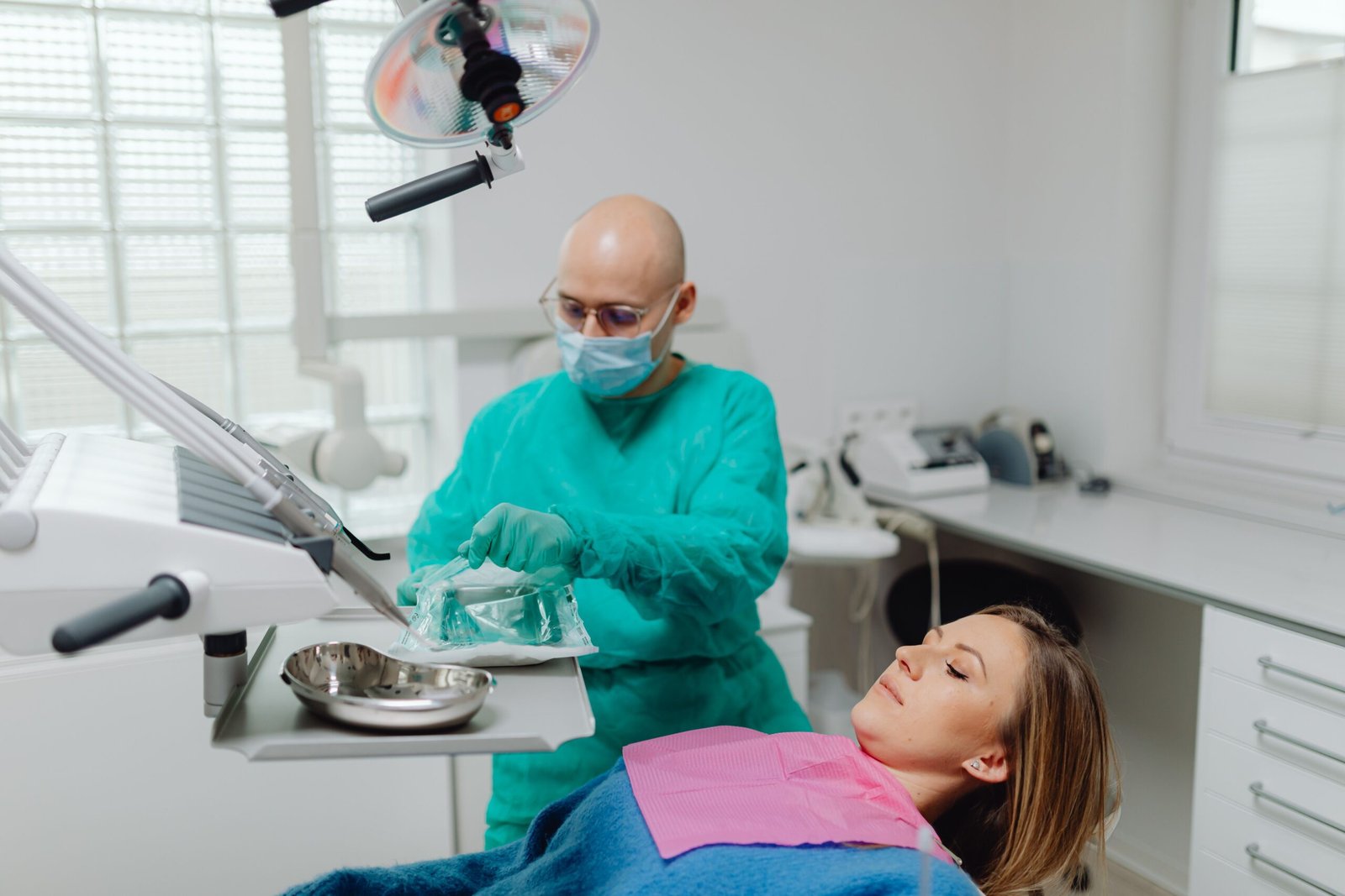 A dentist in latex gloves opens a sterile package of medical instruments in a clinical setting, preparing for a dental procedure.