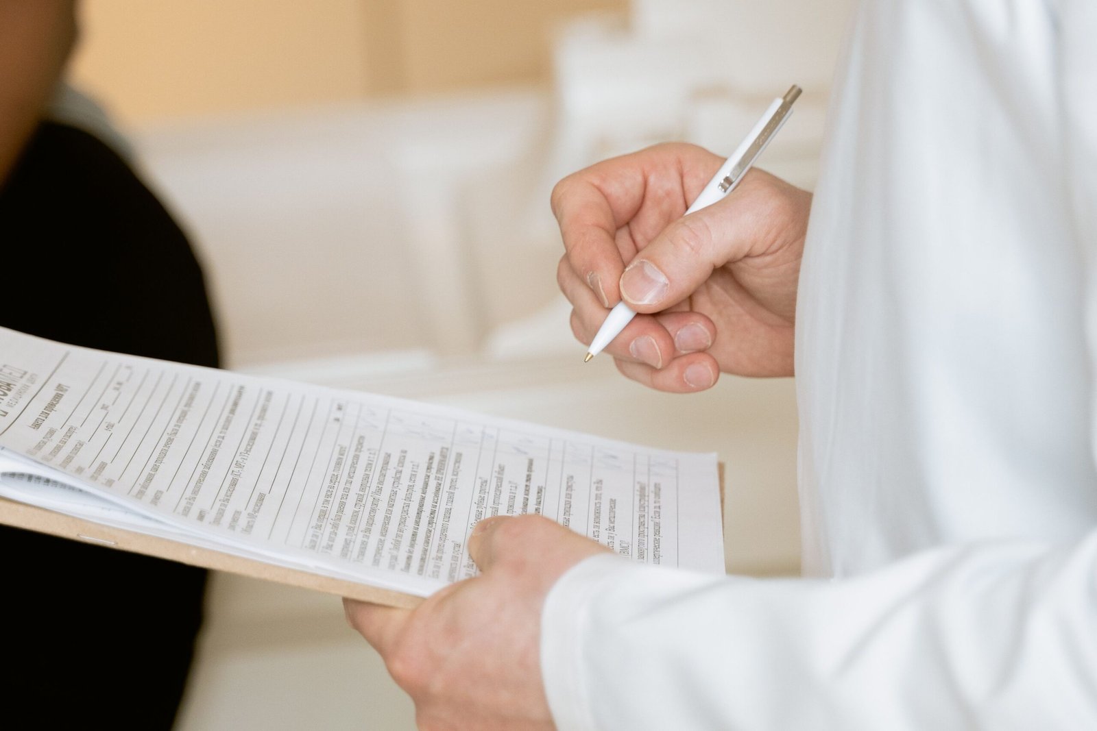 A medical professional wearing a white coat examines a clipboard containing patient documents during a clinical consultation.