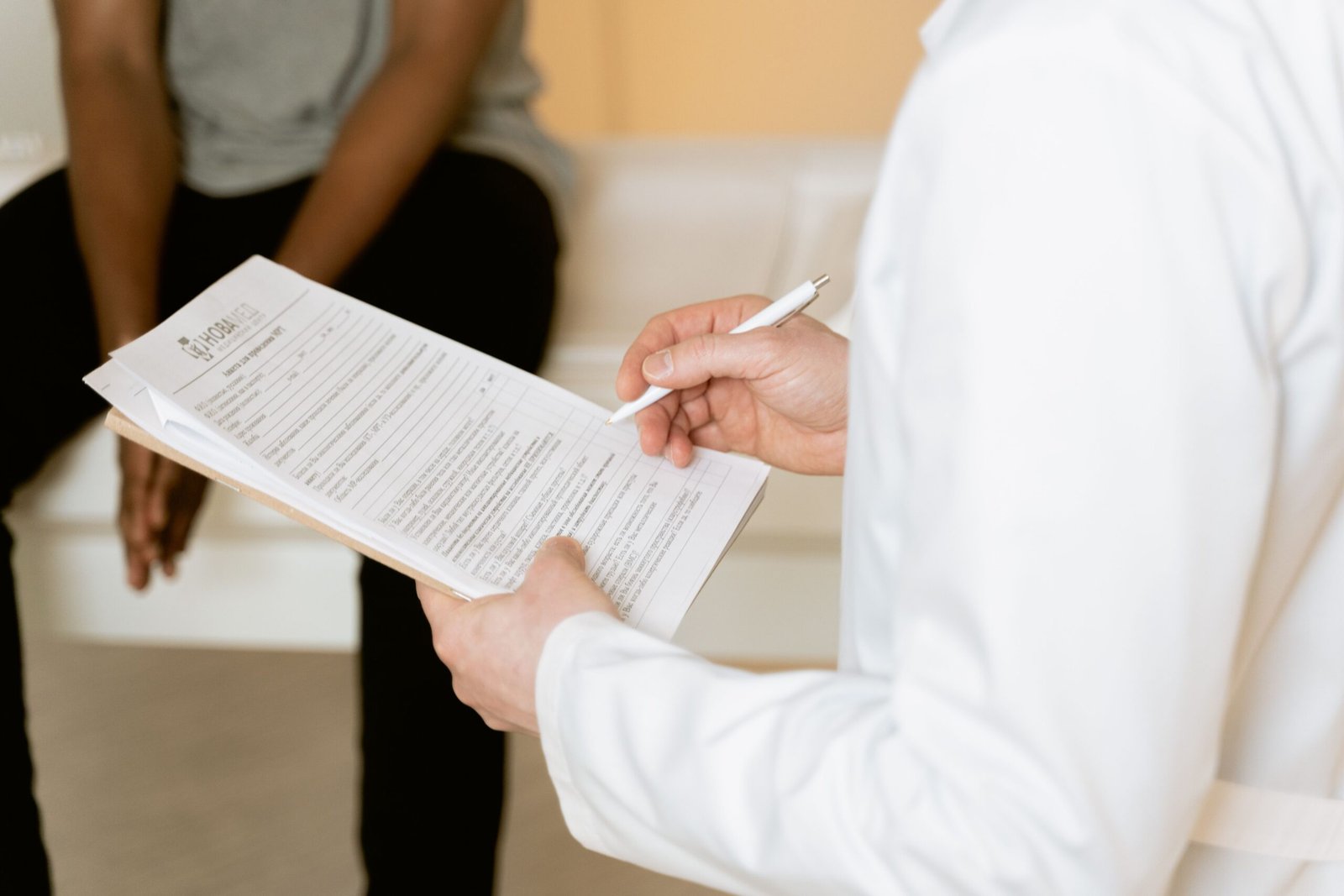 A healthcare professional in a white coat reviews a medical form and takes notes during a patient consultation