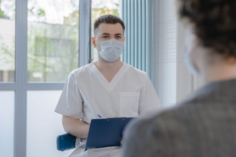 A healthcare professional in scrubs sits across from a patient, taking notes during a consultation about their treatment.