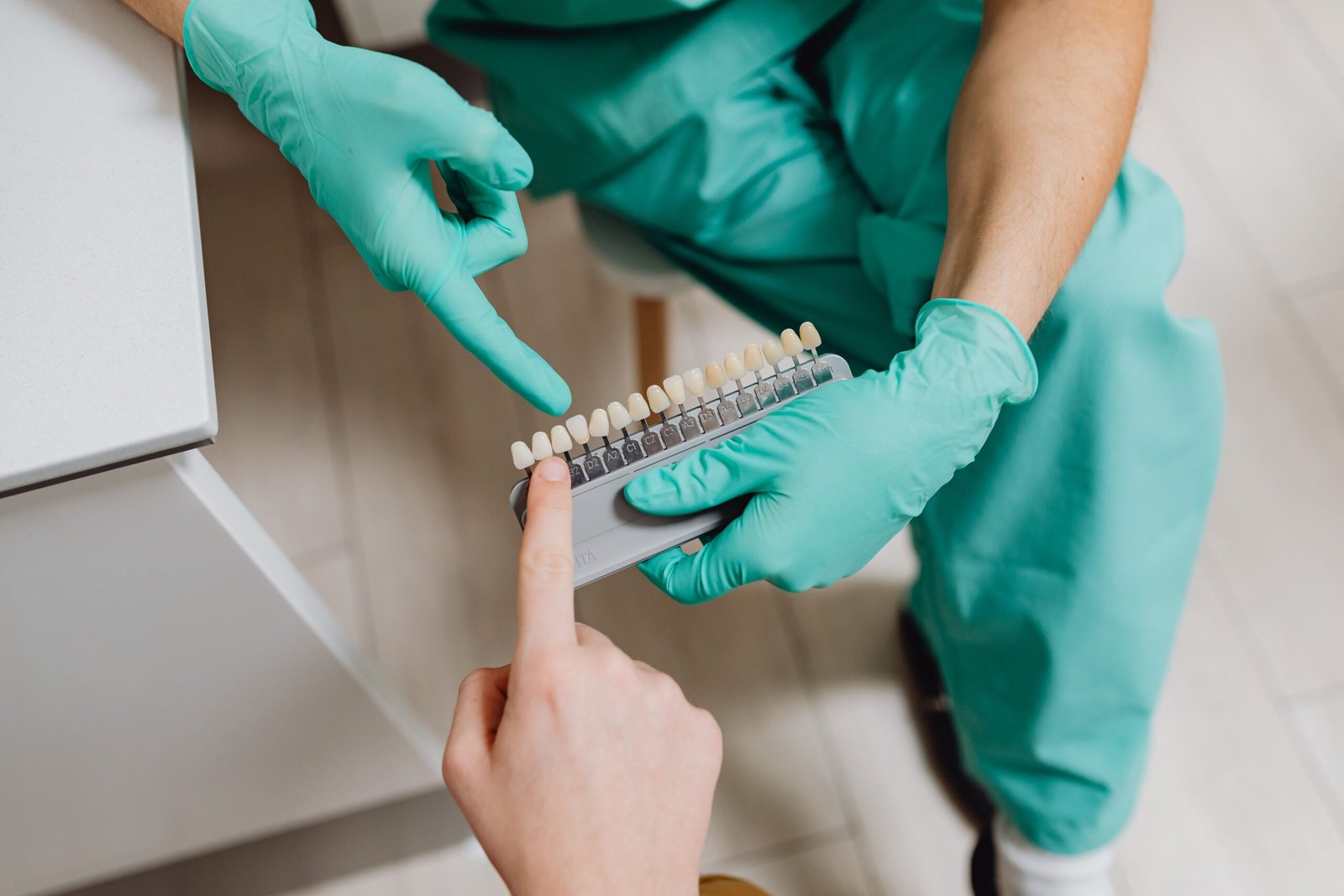 A dental professional in gloves holding a tooth shade guide while assisting a patient