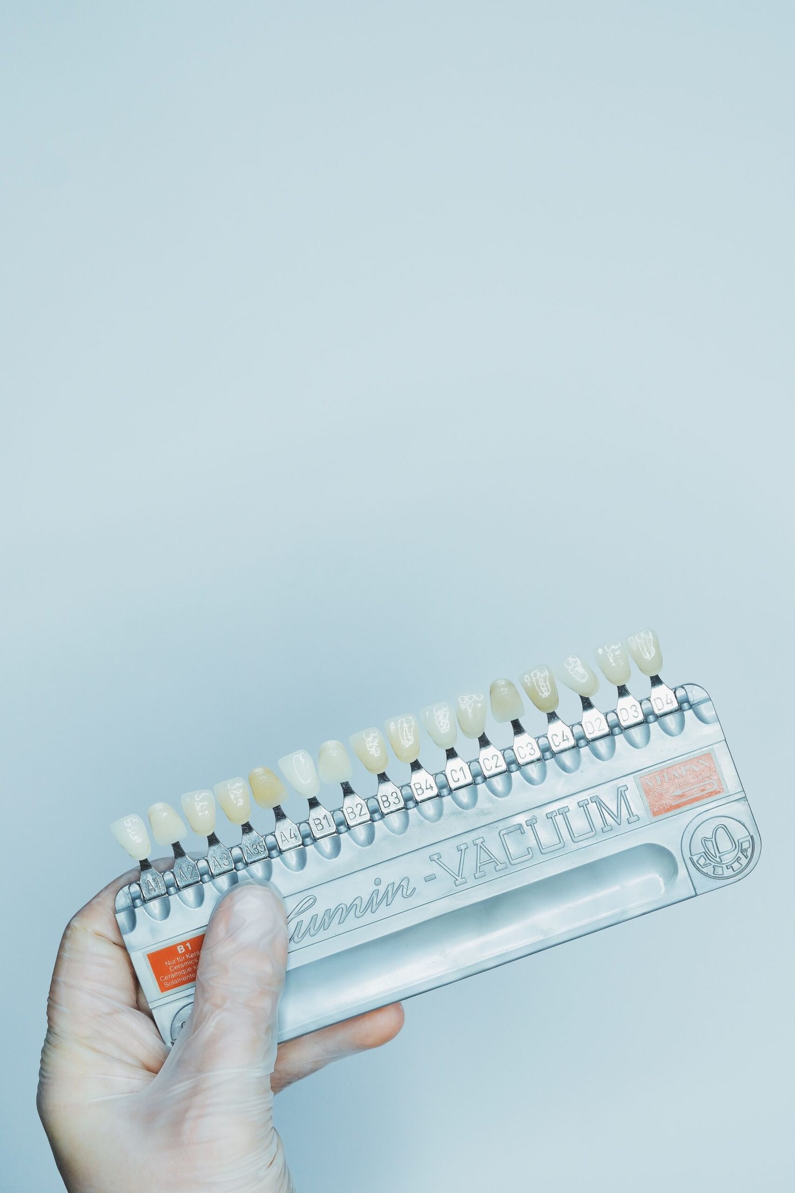 A gloved hand holding a dental shade guide against a light blue background