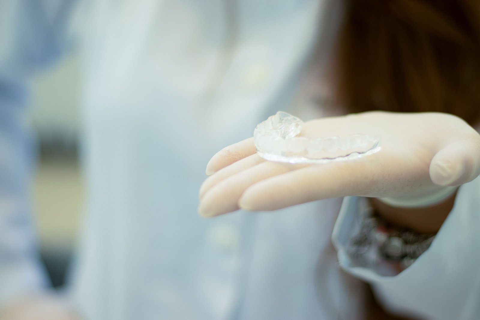 A dentist's gloved hand presenting a transparent mouthguard in a clinical setting