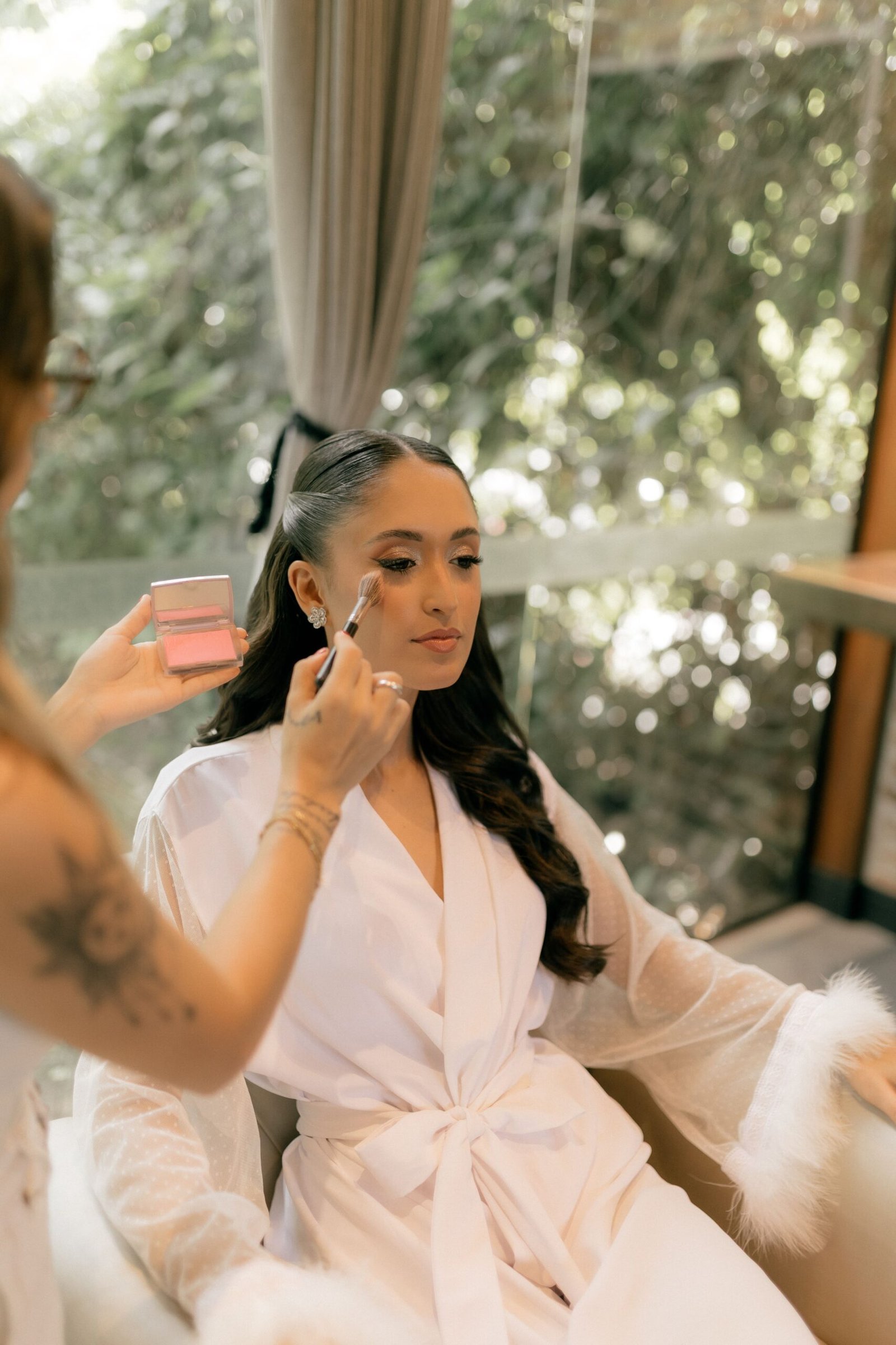 A bride in a white robe having makeup applied before her wedding