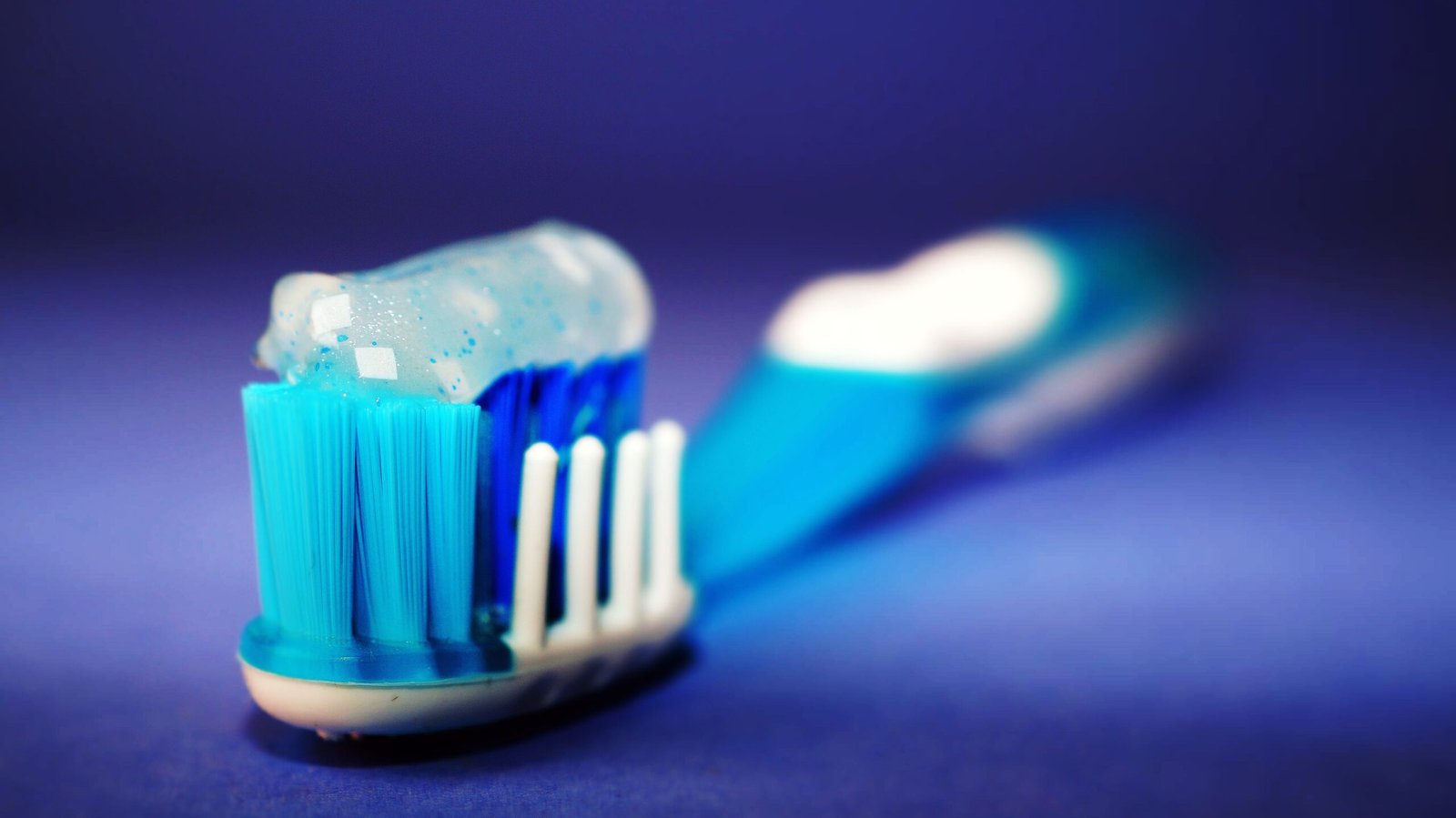 A macro shot of a toothbrush with blue toothpaste against a blurred background.
