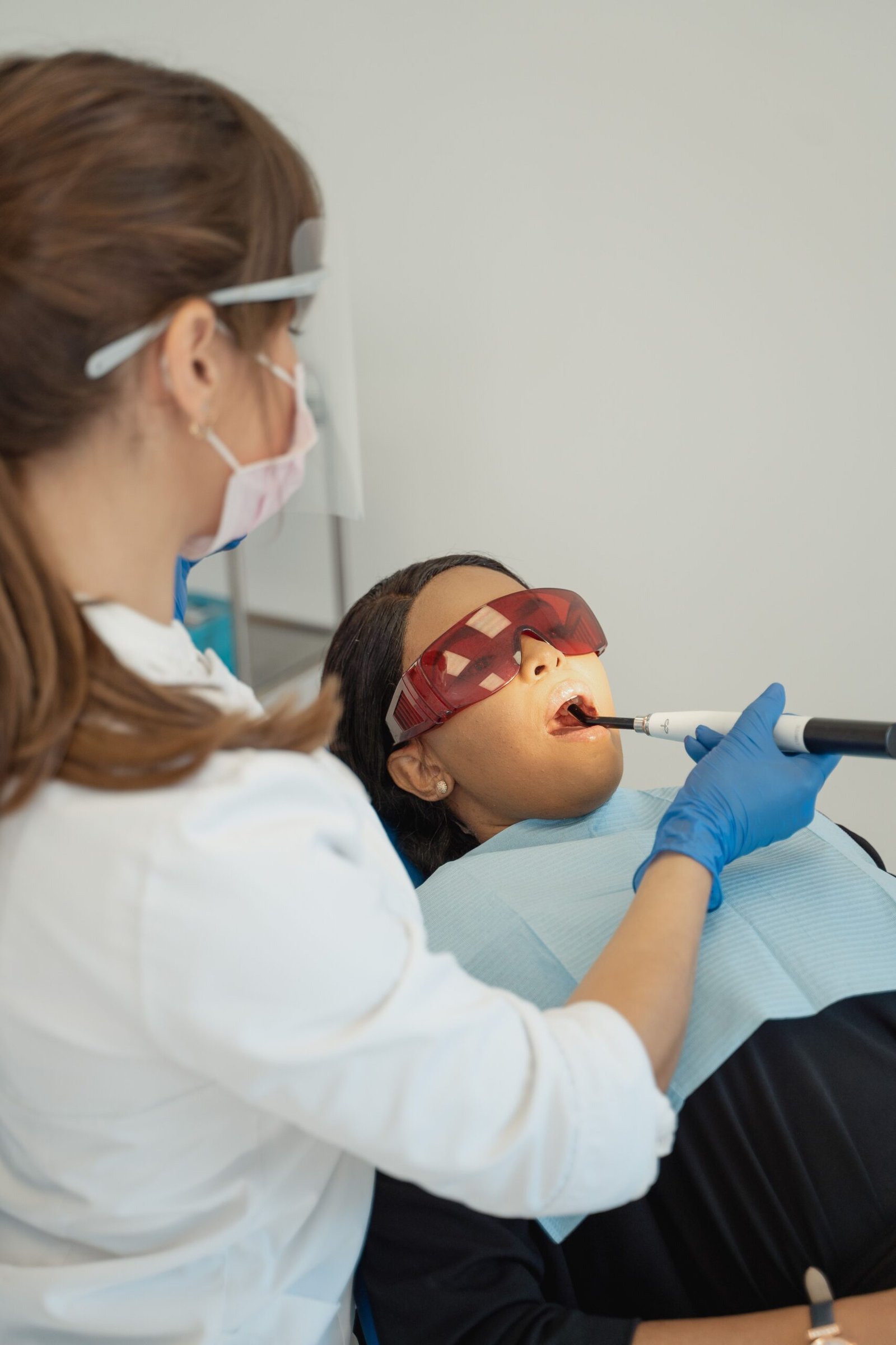A female dentist directing a handheld dental light at a patient's mouth in a modern clinic