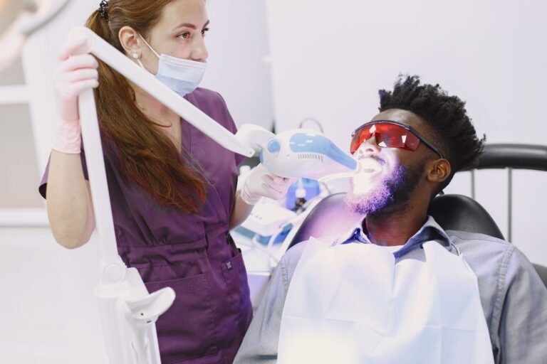 A dentist performing a teeth whitening procedure on a patient using specialized equipment.