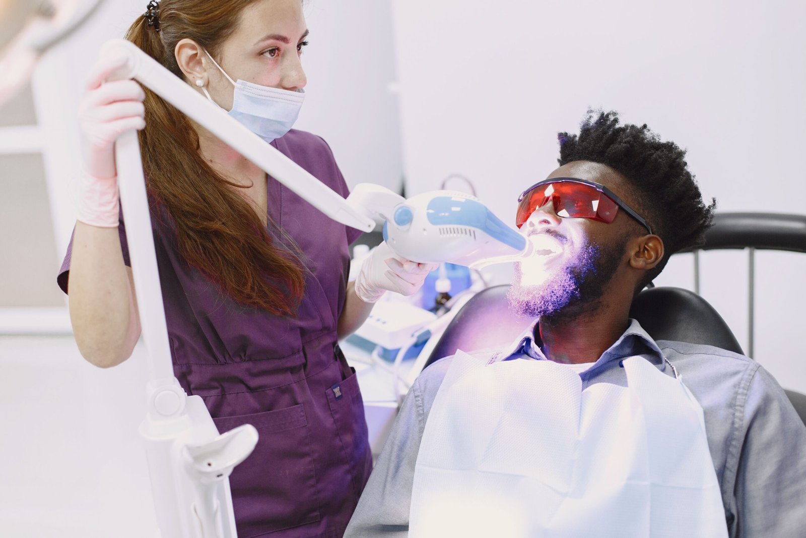 A dentist performing a teeth whitening procedure on a patient using specialized equipment.