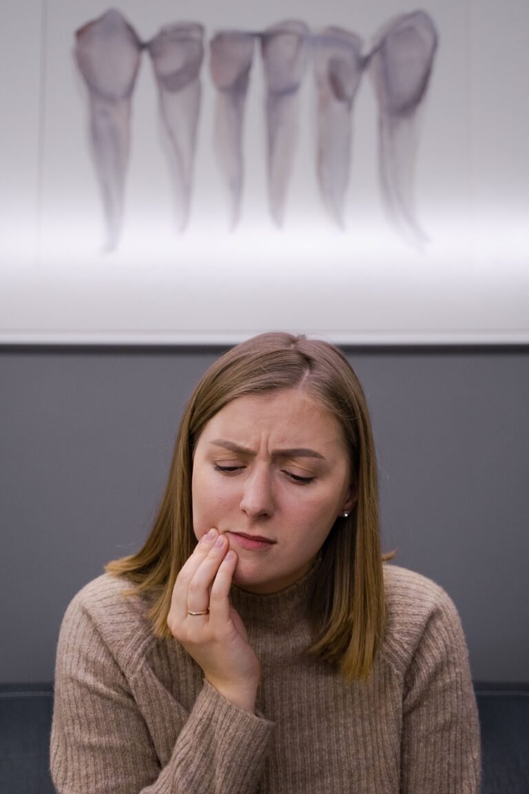A concerned woman holding her cheek because of a toothache while seated in a dental office.