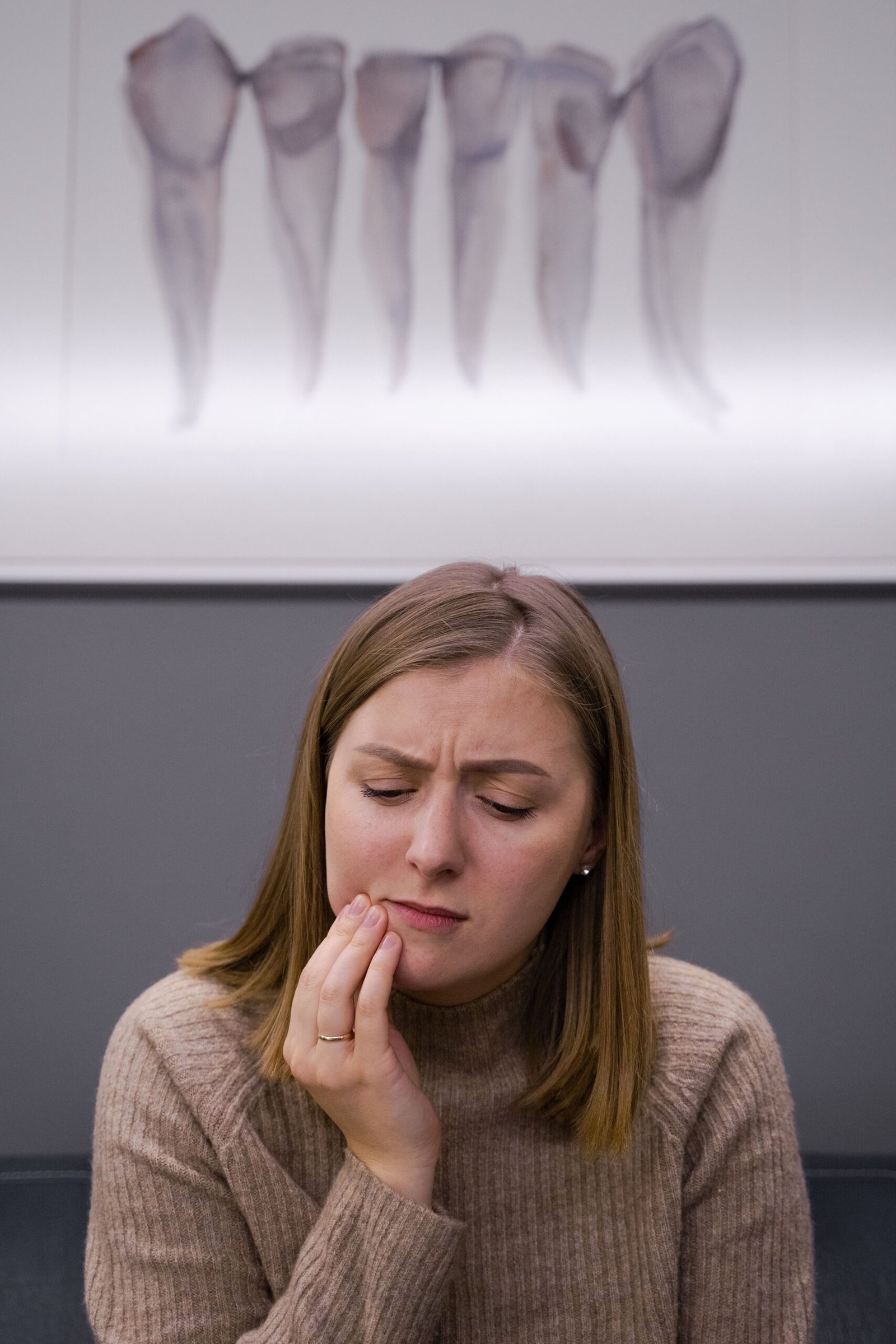 A concerned woman holding her cheek because of a toothache while seated in a dental office.