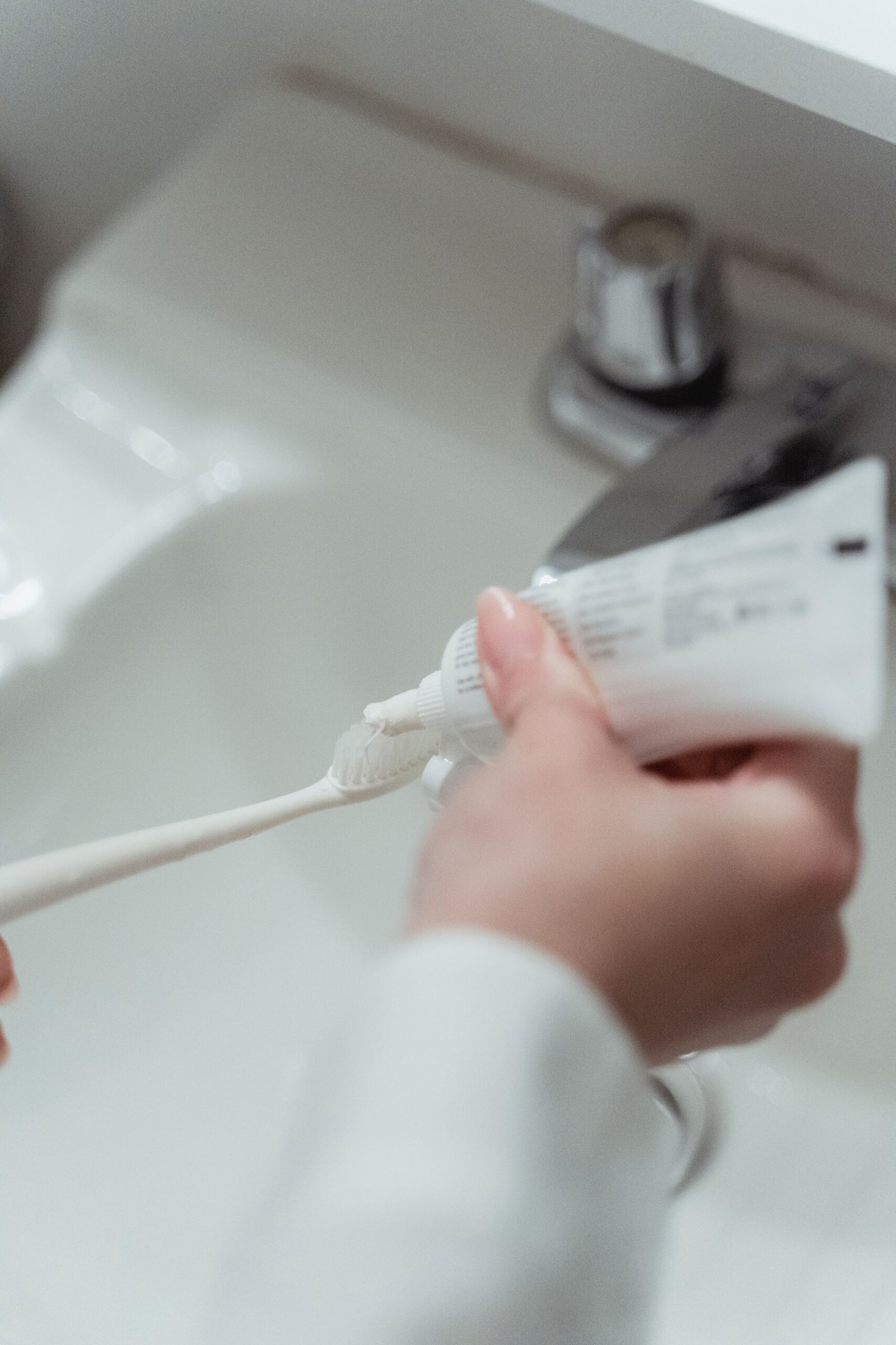 A close-up of a hand squeezing toothpaste onto a toothbrush at the sink
